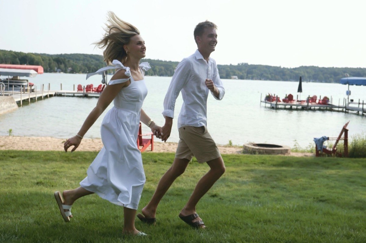 Tucker and Syd running hand in hand across a lakeside lawn