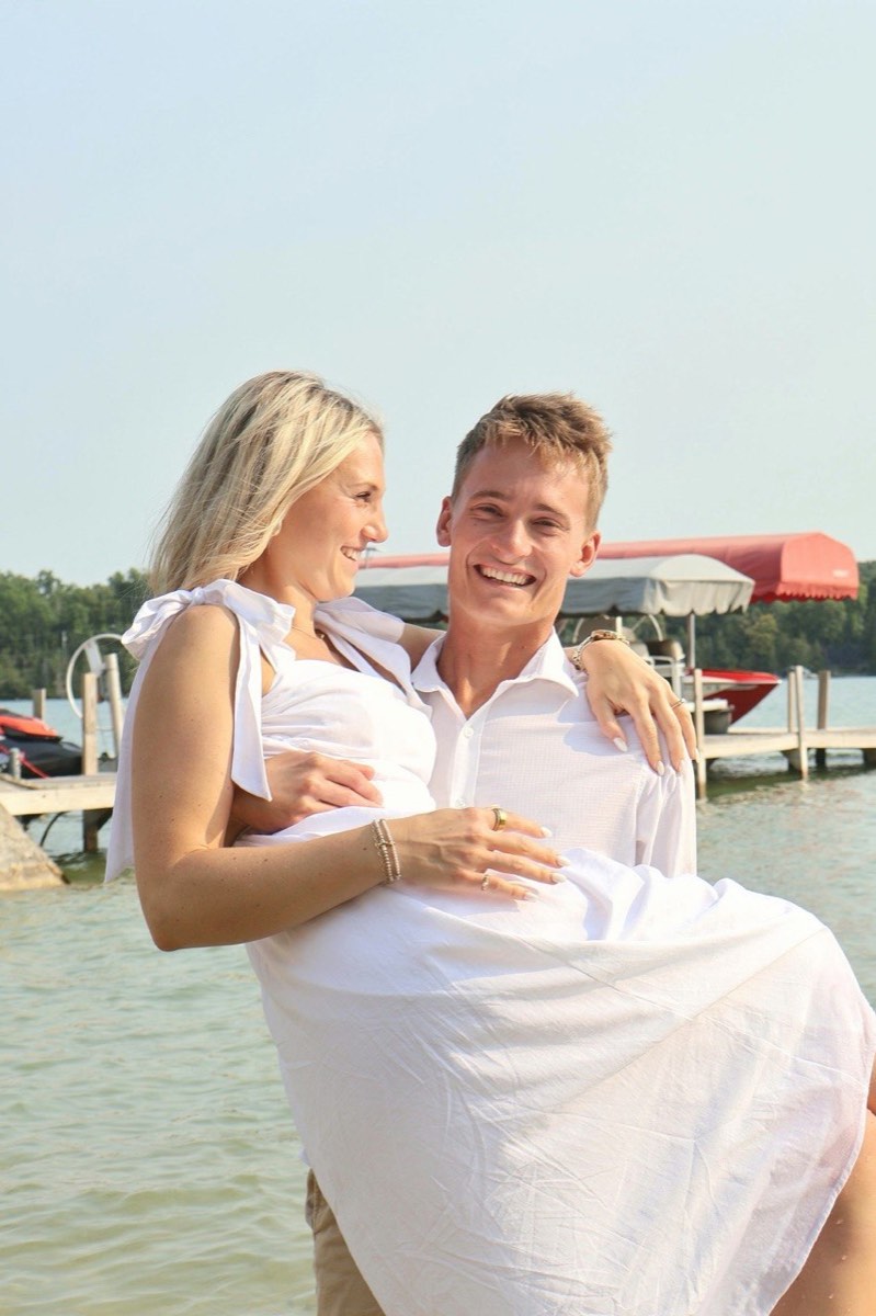 Tucker carrying Syd while both laugh beside the lake