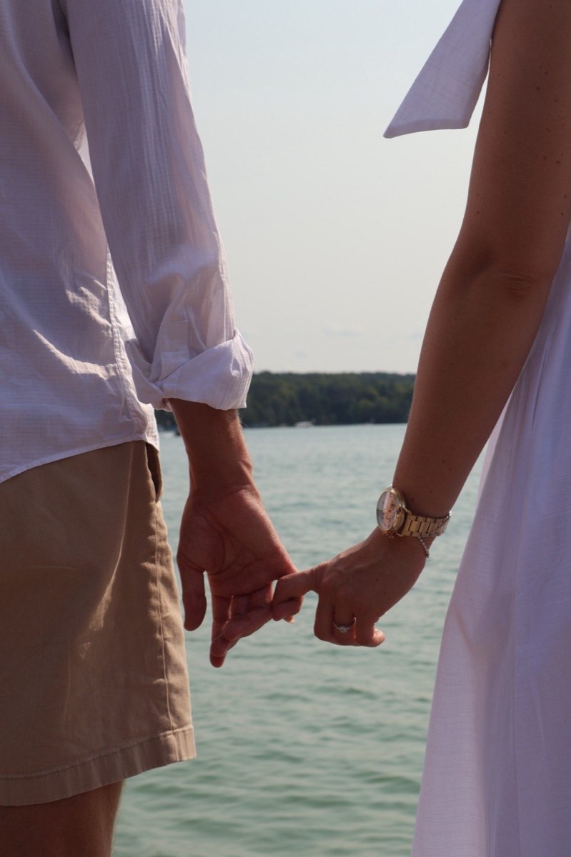 Close-up of Tucker and Syd linking hands with the lake behind them