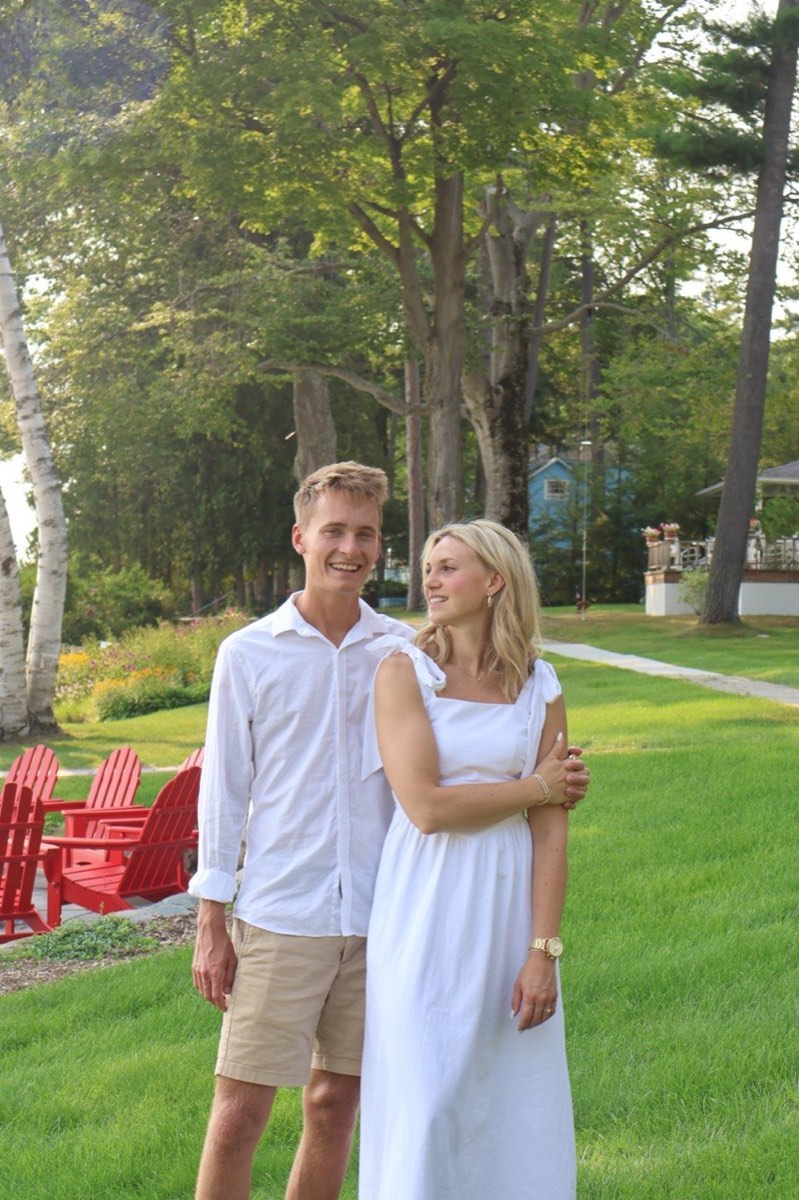 Tucker and Syd standing together on a green lakeside lawn